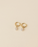 Gold earrings with pearl drops on a beige background