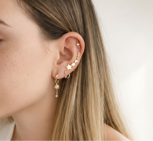 Close-up of a person wearing gold star-shaped earrings with a neutral background