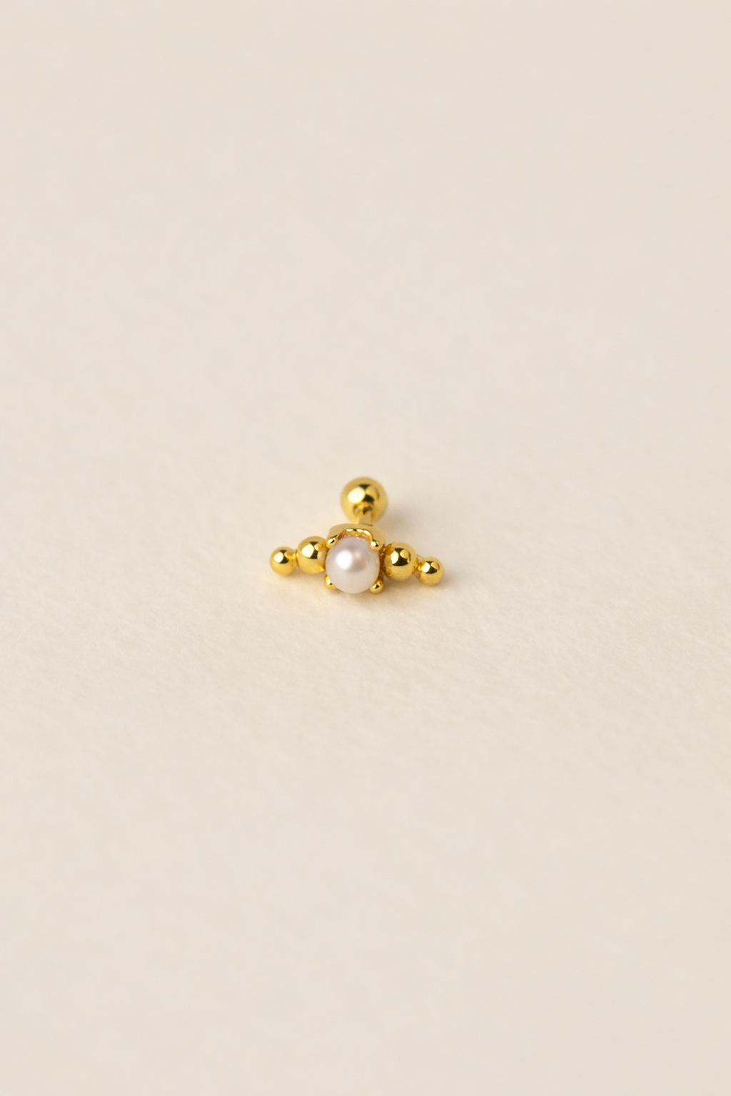 Gold earring with a central pearl on a beige background