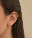 Close-up of an ear wearing a gold earring with a beige background