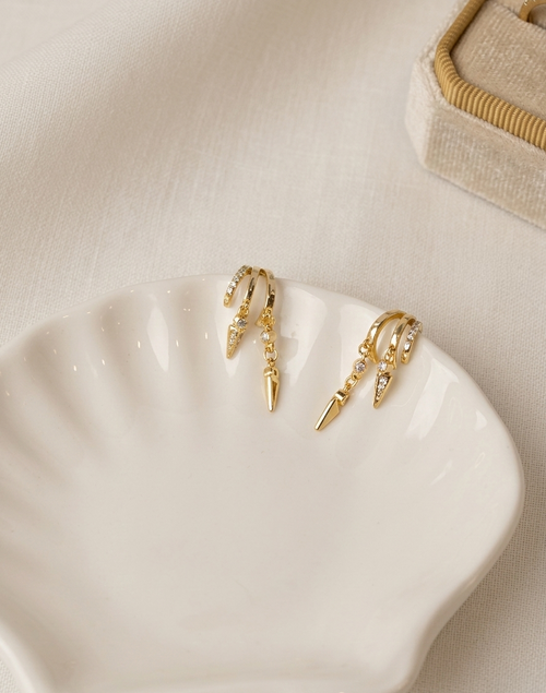 Gold hoop earrings with dangling elements on a white dish.