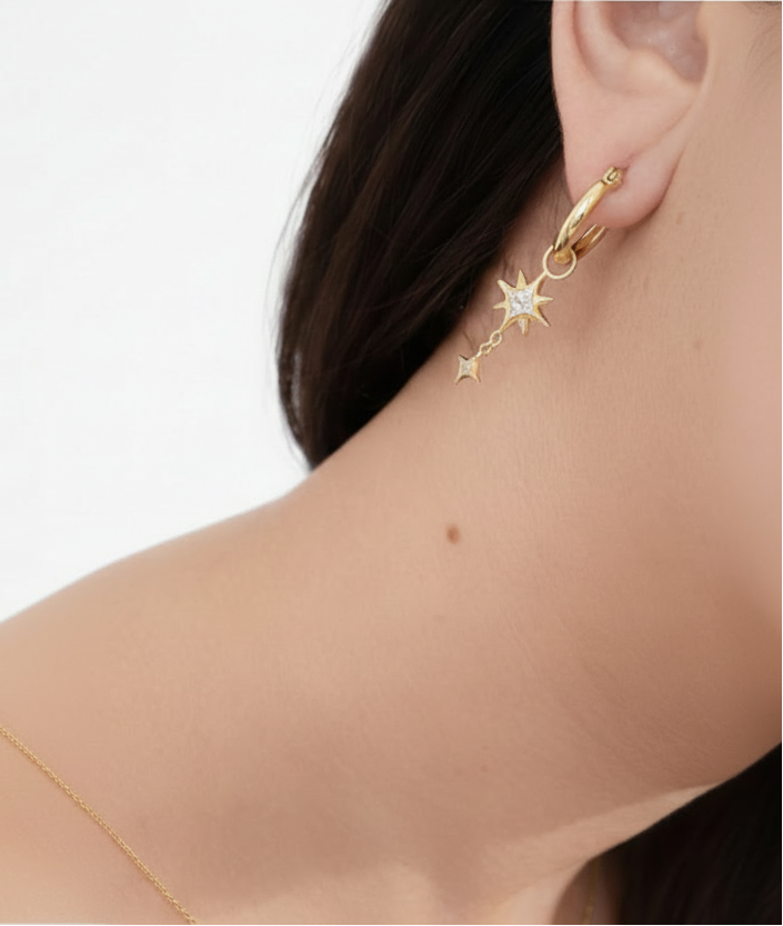 Gold star-shaped earring worn by a person on a white background