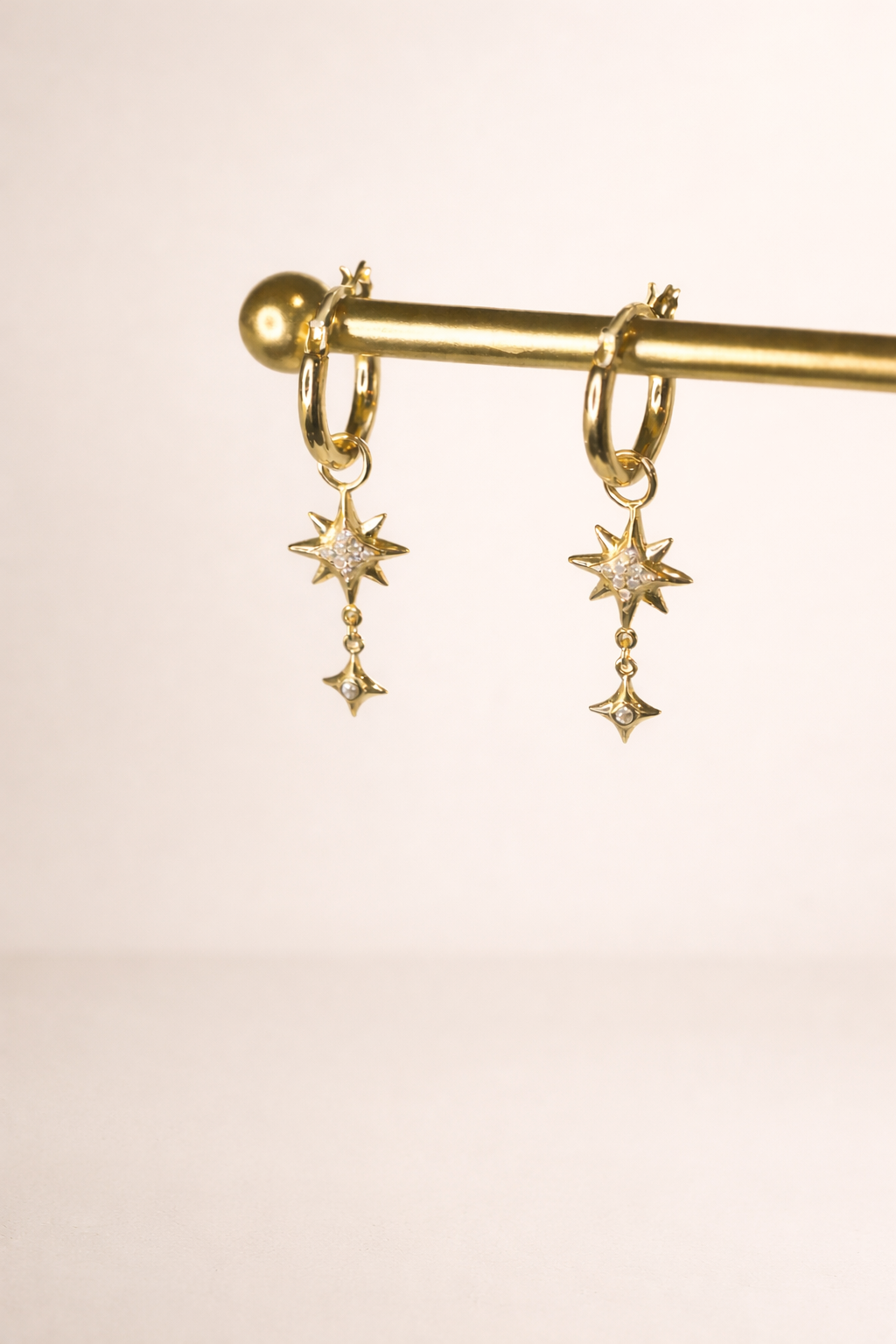 Gold hoop earrings with star-shaped charms on a gold rod against a beige background