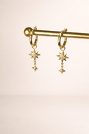 Gold hoop earrings with star-shaped charms on a gold rod against a beige background