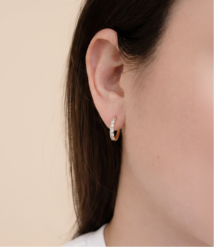 Close-up of an ear wearing a small hoop earring with a white background