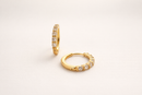 Gold hoop earrings with embedded stones on a light beige background