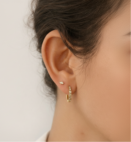 Close-up of a person wearing gold hoop earrings with a neutral background