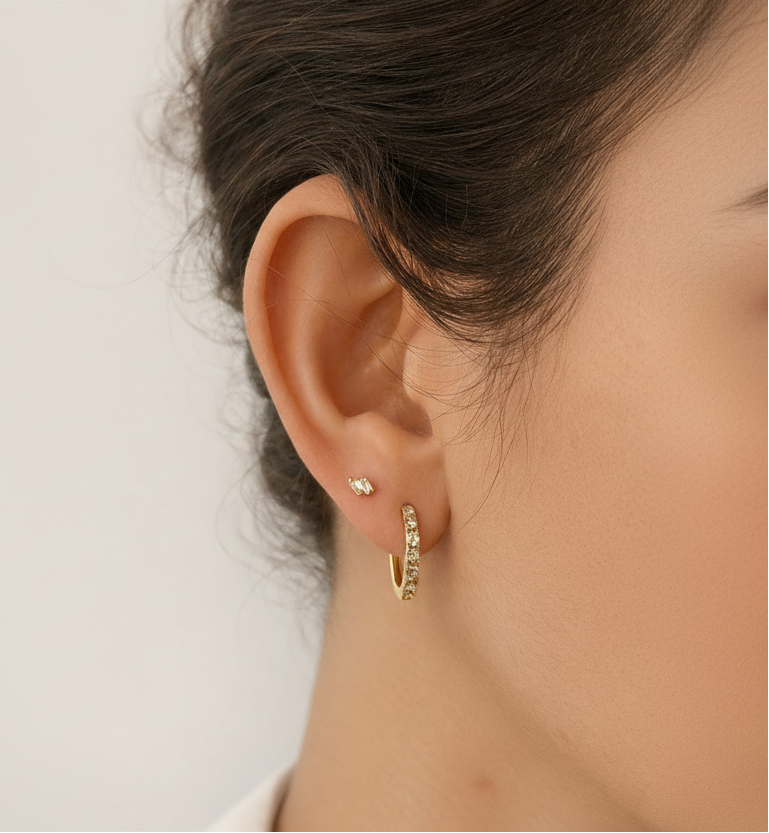 Close-up of a person wearing gold hoop earrings with a neutral background
