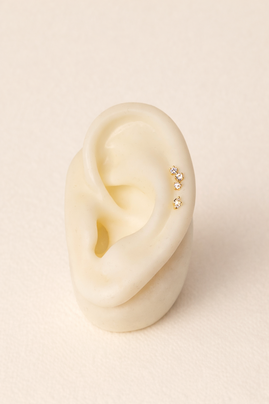 Close-up of an ear wearing a gold earring on a beige background