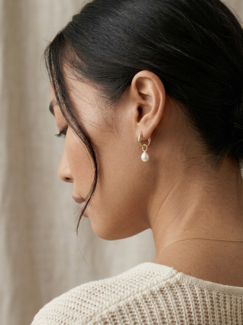 Close-up of a woman wearing pearl earrings with a neutral background
