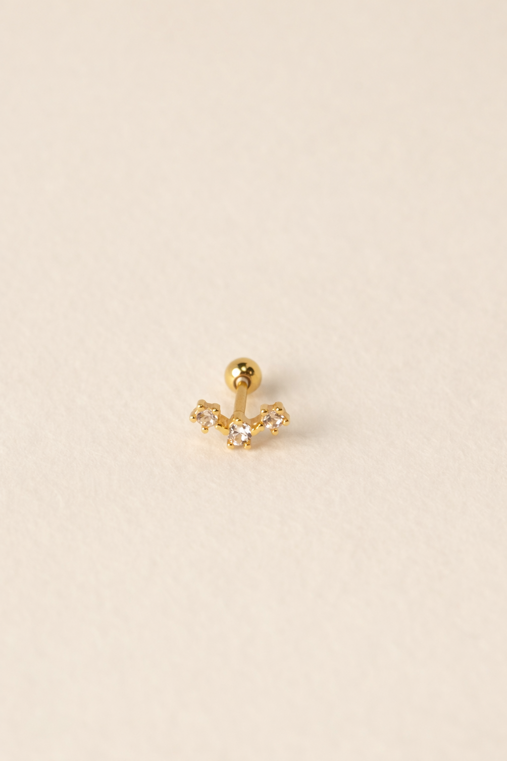 Gold earring with a small gemstone on a beige background