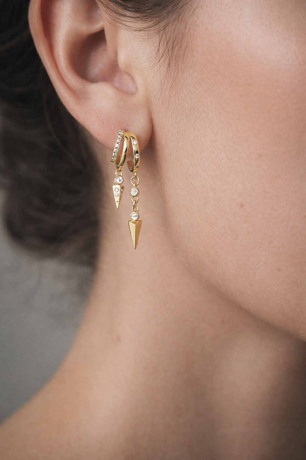 Close-up of a person wearing gold earrings with dangling elements.