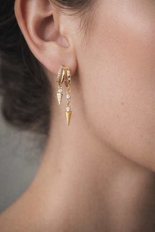 Close-up of a person wearing gold earrings with dangling elements.